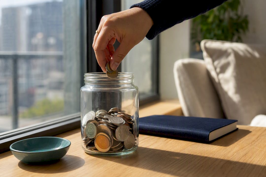 Hand adding coins to emergency fund jar